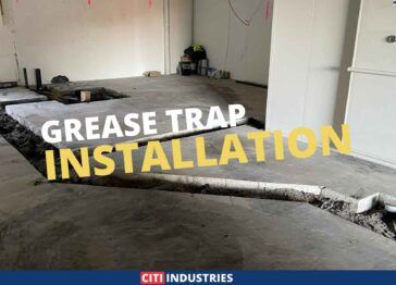 Grease trap installation in progress at a new bakery. The image shows a partially completed concrete floor with trenches dug out for the placement of the grease trap and drainage system. Electrical wiring and equipment are visible in the background, and the project is marked with the Citi Industries logo